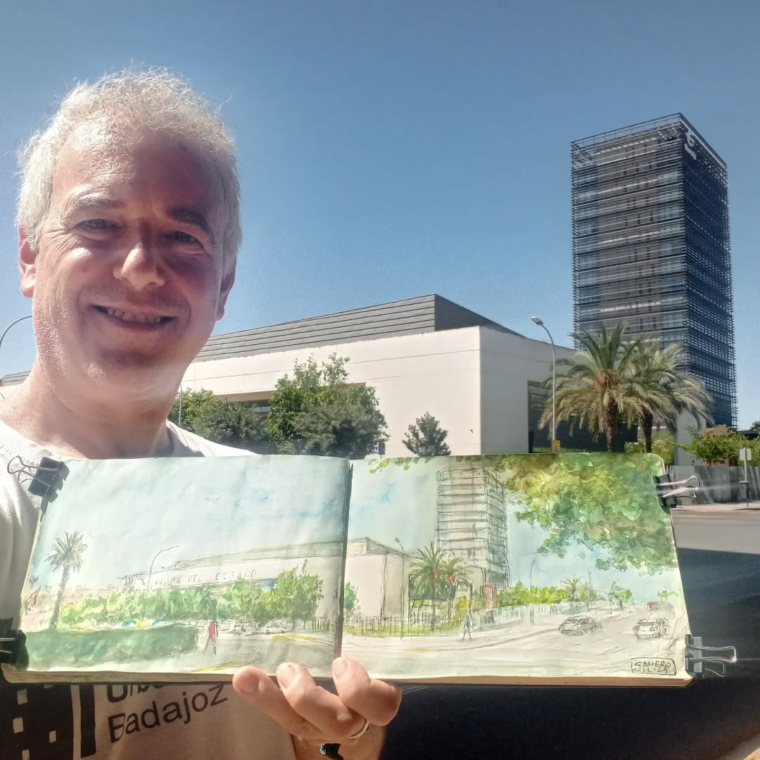 Gamero Gil mostrando su cuaderno de dibujo frente a un paisaje urbano